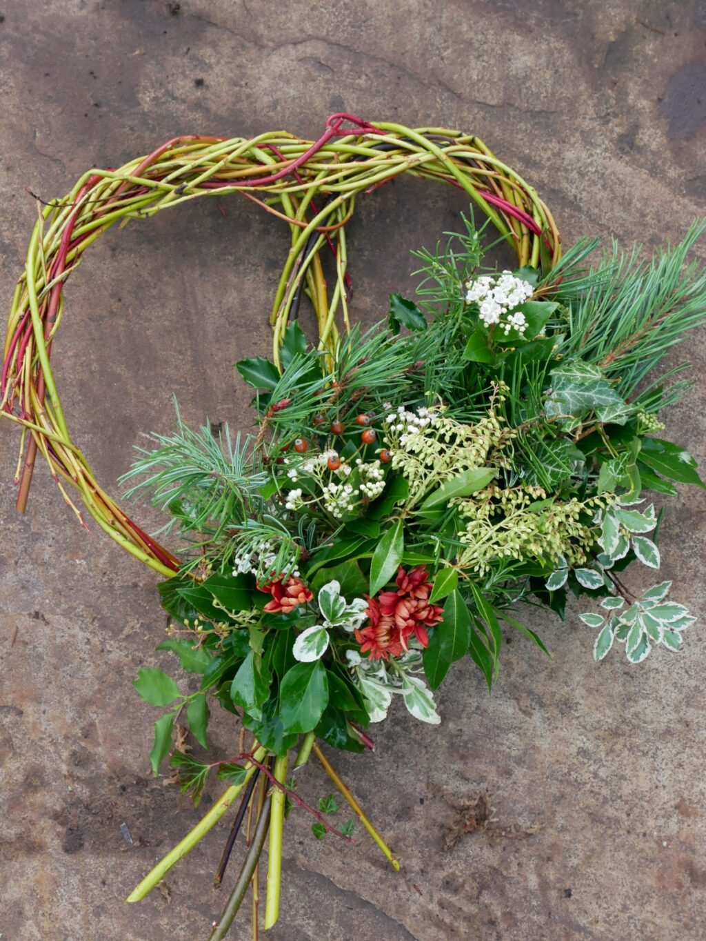 A woven willow heart wreath adorned with evergreen foliage and winter blossom