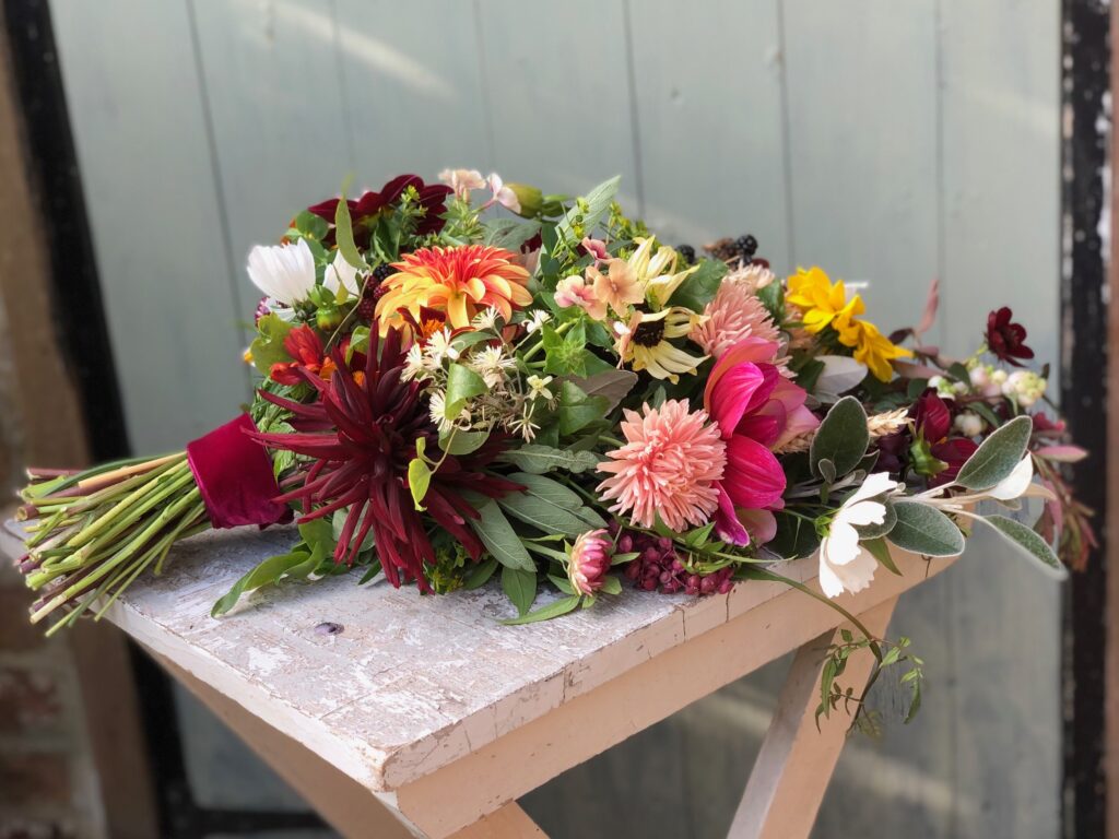 Colourful autumn sheaf with dahlias by Blackbird Garden sits on a wooden table in front of a painted door.