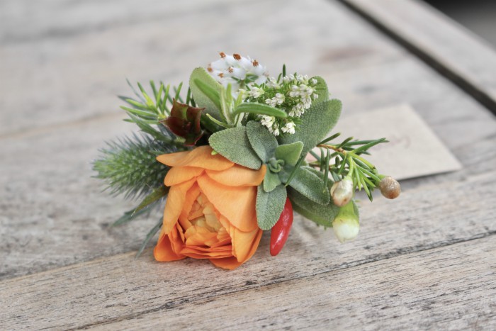 A spring buttonhole with sage and rosemary and chilli with an orange ranunculus for a keen cook