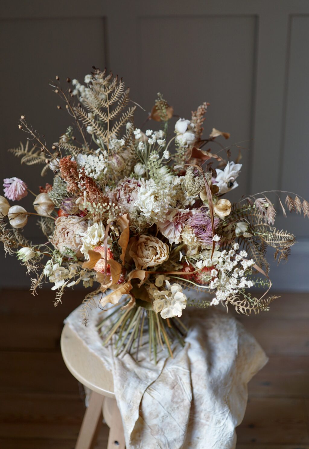 An everlasting flower bouquet in autumn colours of pale pink, bronze and white stands on a small table.