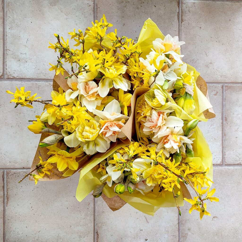 A bucket filled with wrapped posies of sunny yellow daffodils, narcissus and forsythia by The Garden Gate Southwold