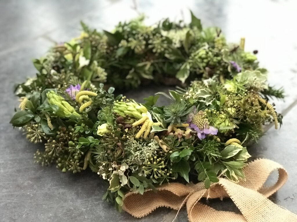 An understated woven wreath is decorated with tree ivy and catkins and a rustic hessian bow by Little Park Flowers.
