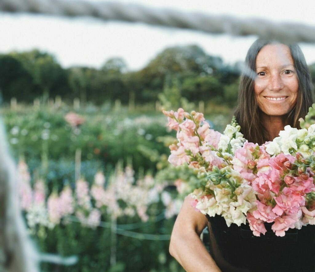 Marie-Claire, flower grower and florist at Love and Honor, holds a bucket of locally grown pink and white snapdragons in her flower plot.