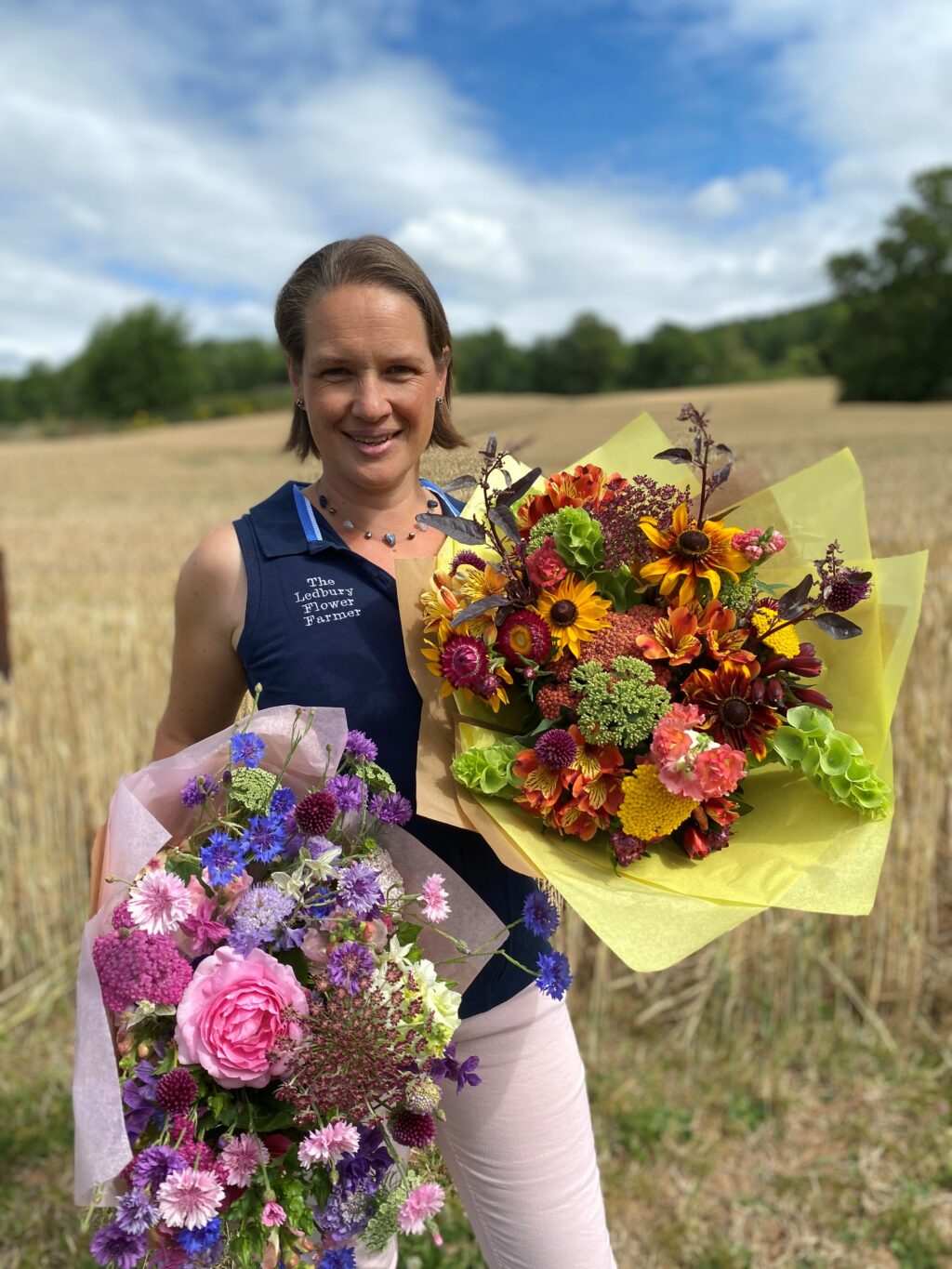 Rozanne Delamore of The Ledbury Flower Farmer holding two stunning bouquets of her flowers against the rural backdrop of her flower farm