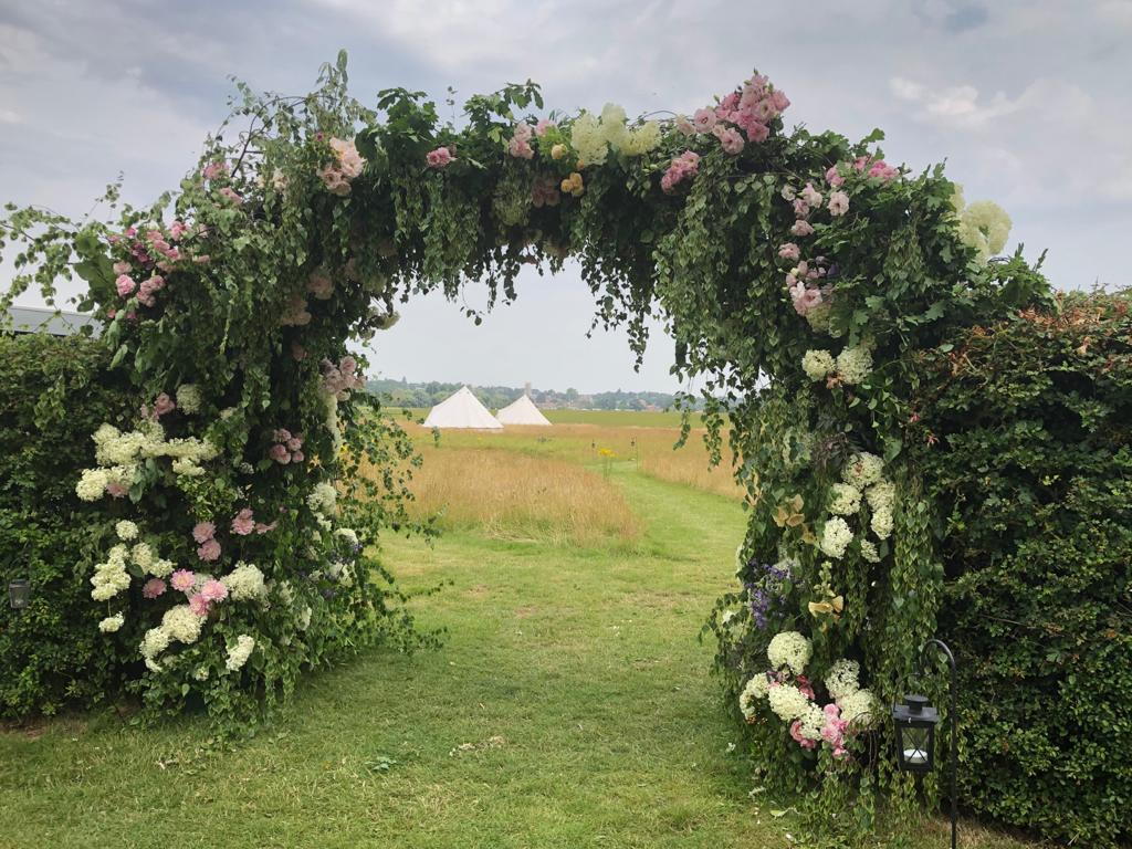 A wild and romantic floral arch by Moat Farm Flowers beautifies the entrance to a wedding venue