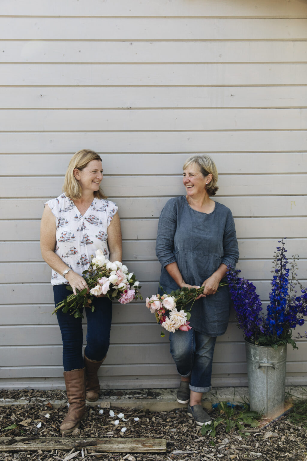 Organic Blooms Jo and Wendy relax against a painted clapboard wall.