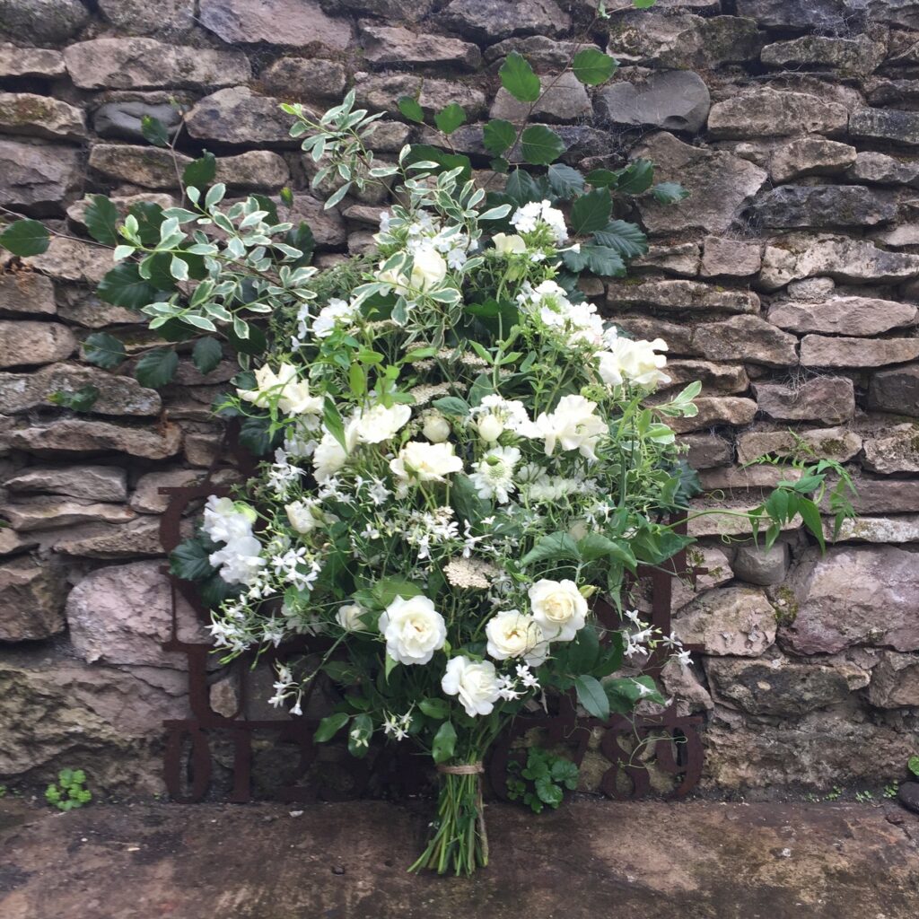 A white summer sheaf by Picking Posies leans against a dry stone wall.
