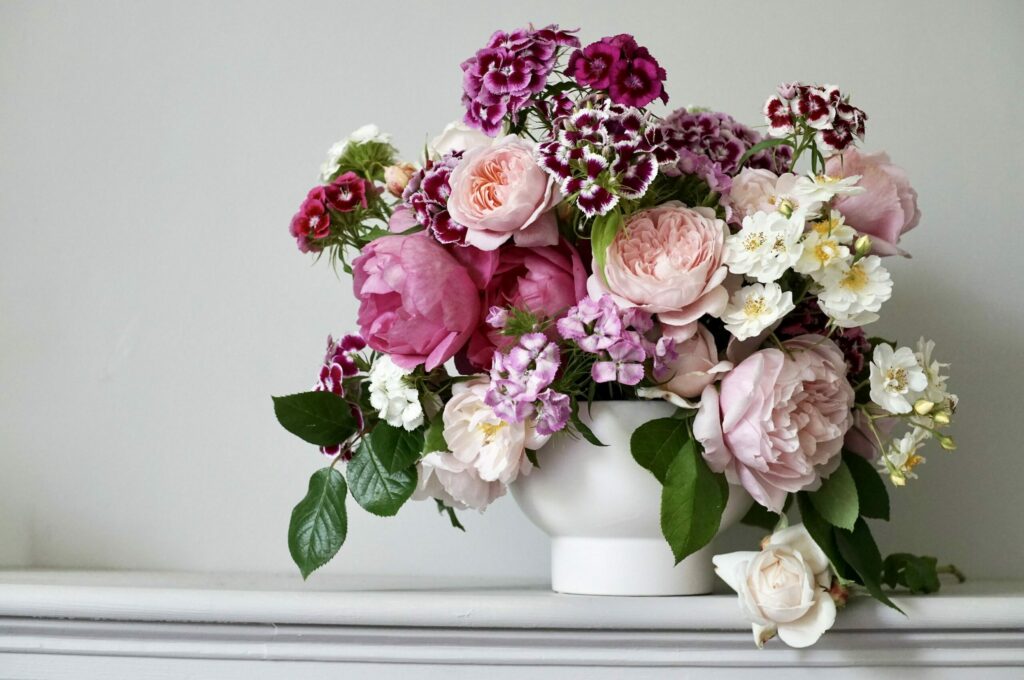 Roses and sweet William flowers in colours of pink and white, arranged in a white bowl, sitting on a grey shelf