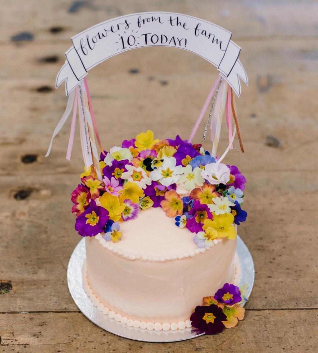 A 10th birthday cake for Flowers from the Farm, decorated with edible flowers by Tallulah Rose Flower School. The edible flowers are primulas from Maddocks Organics.