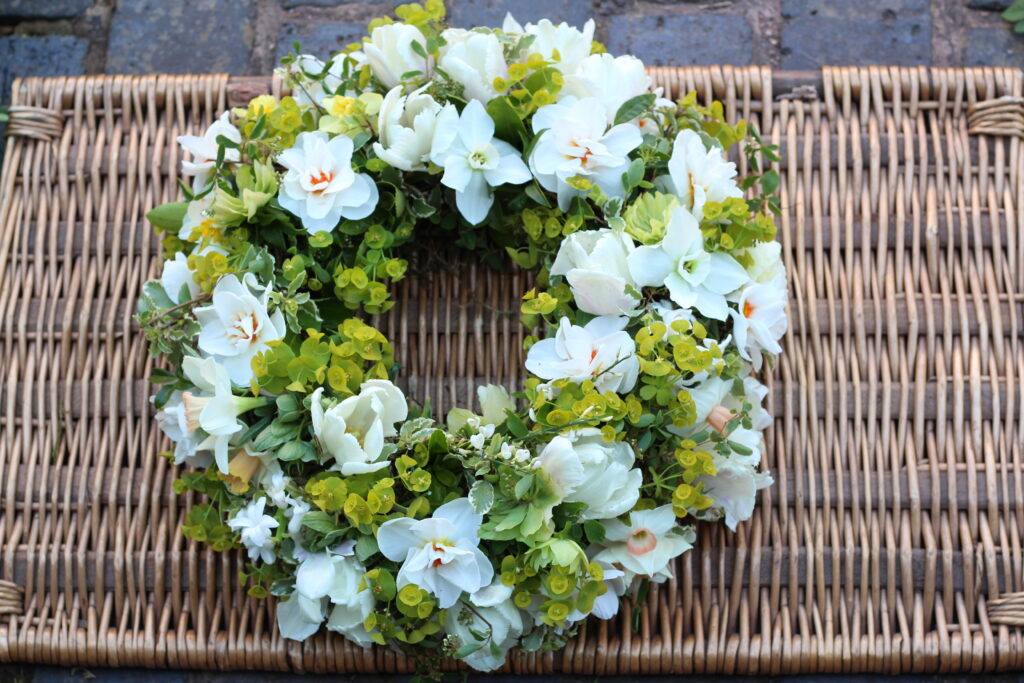 A spring wreath in whites and greens with narcissi, tulips and euphorbia. Natural Funeral flowers by Tuckshop Flowers, Birmingham.
