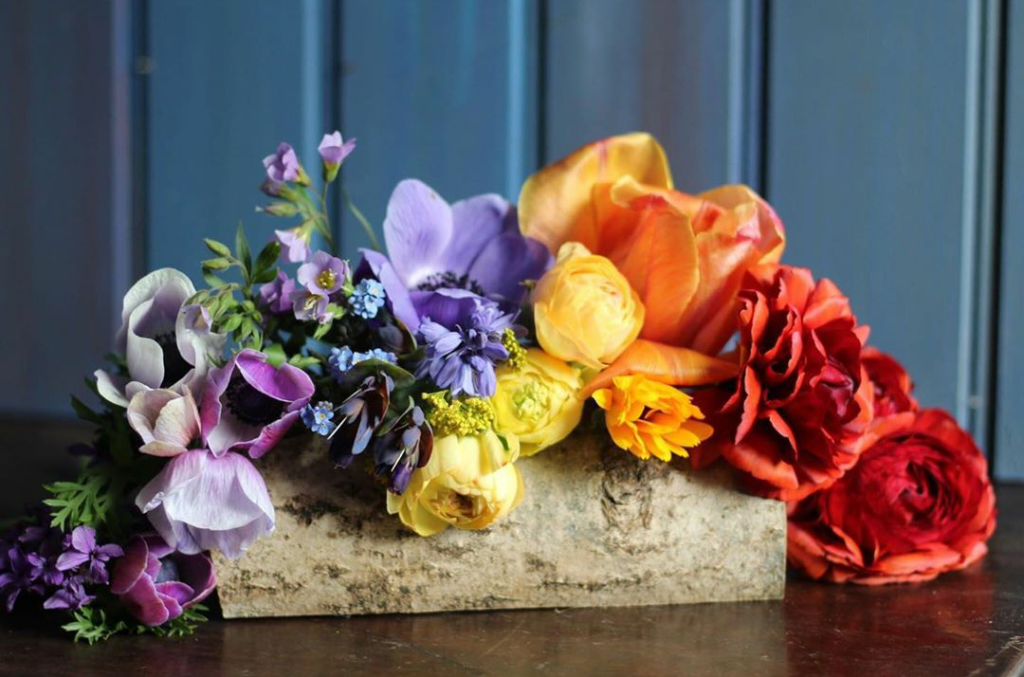 A rainbow of flowers arranging in a wooden container by Wildly Beautiful Flowers